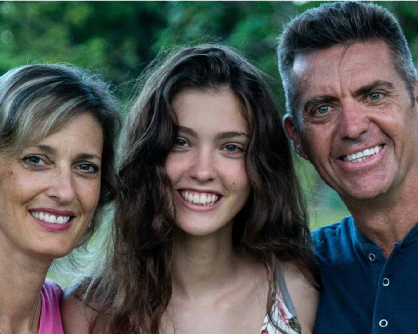 photo of couple and daughter smiling at camera behind green scenery