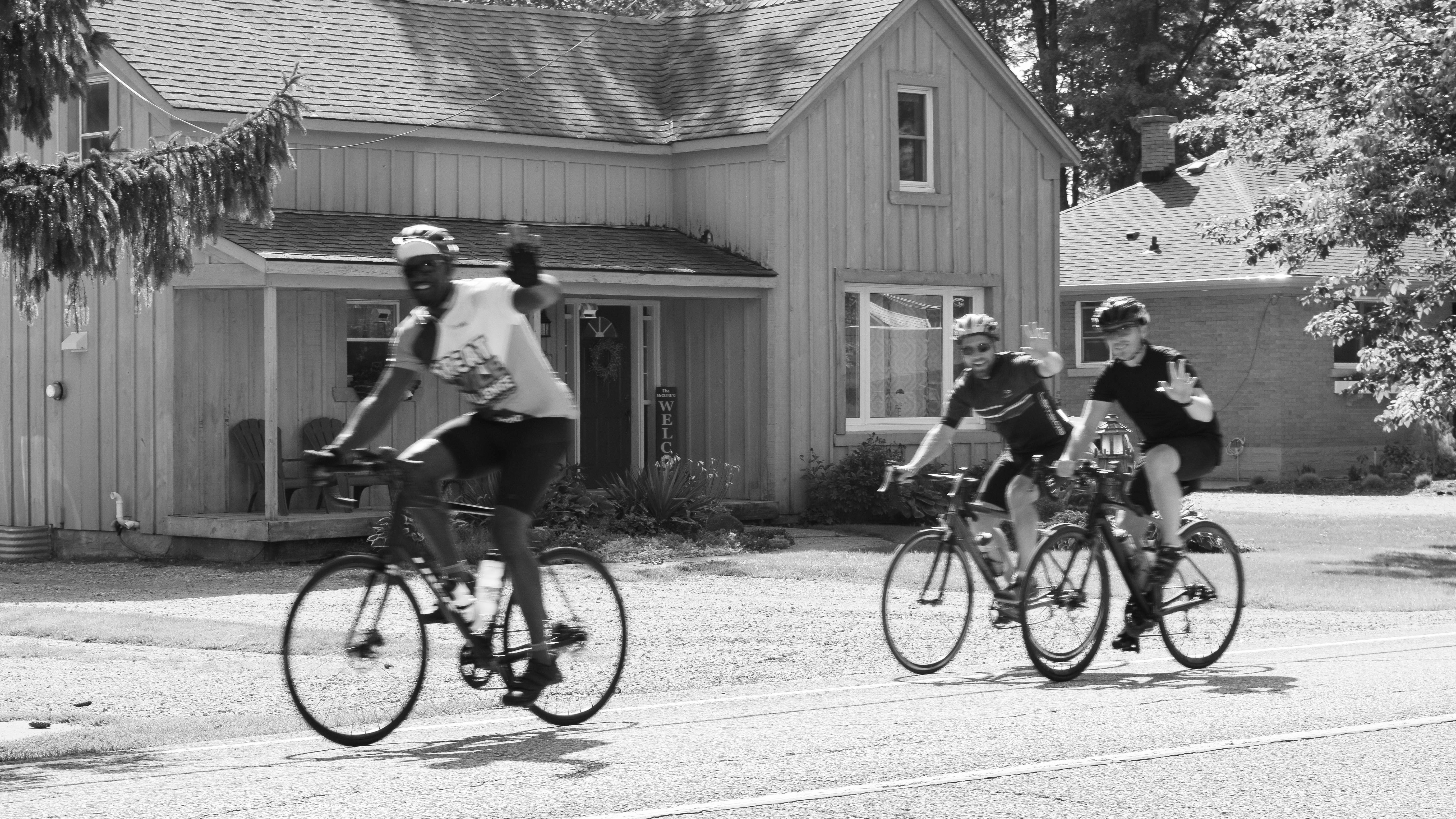 Photo of a group of bikers waving at the camera in black and white.