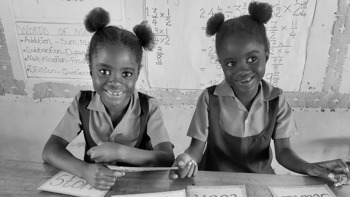 Black and white photo of two VOH Africa girls at a school desk smiling at the camera.