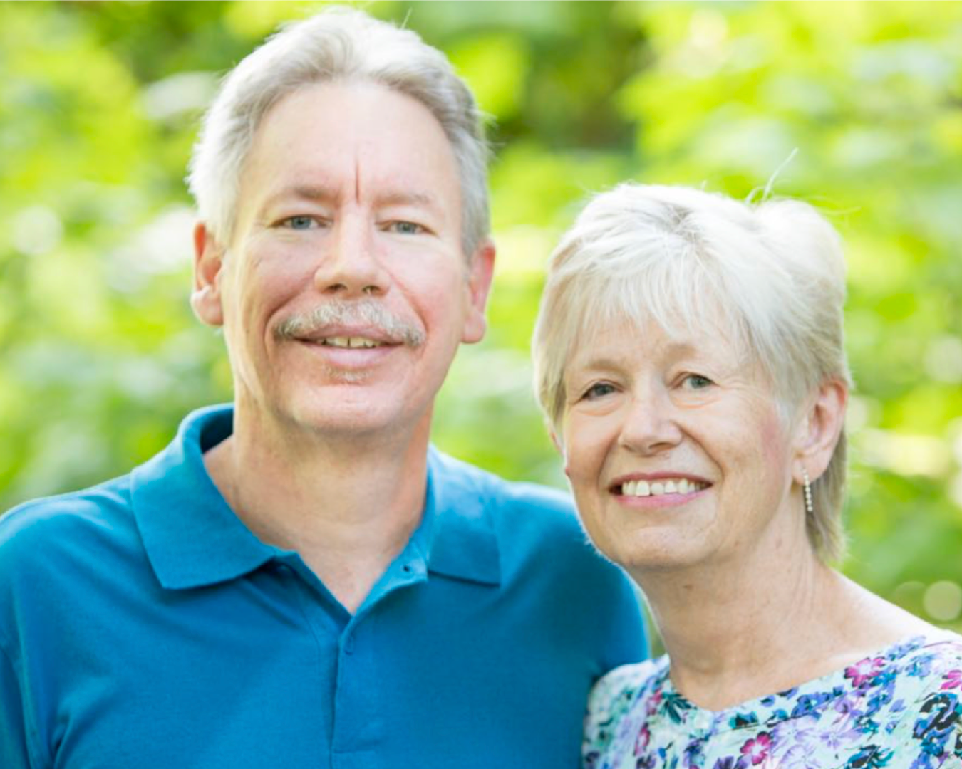 couple smiling at camera behind greenery