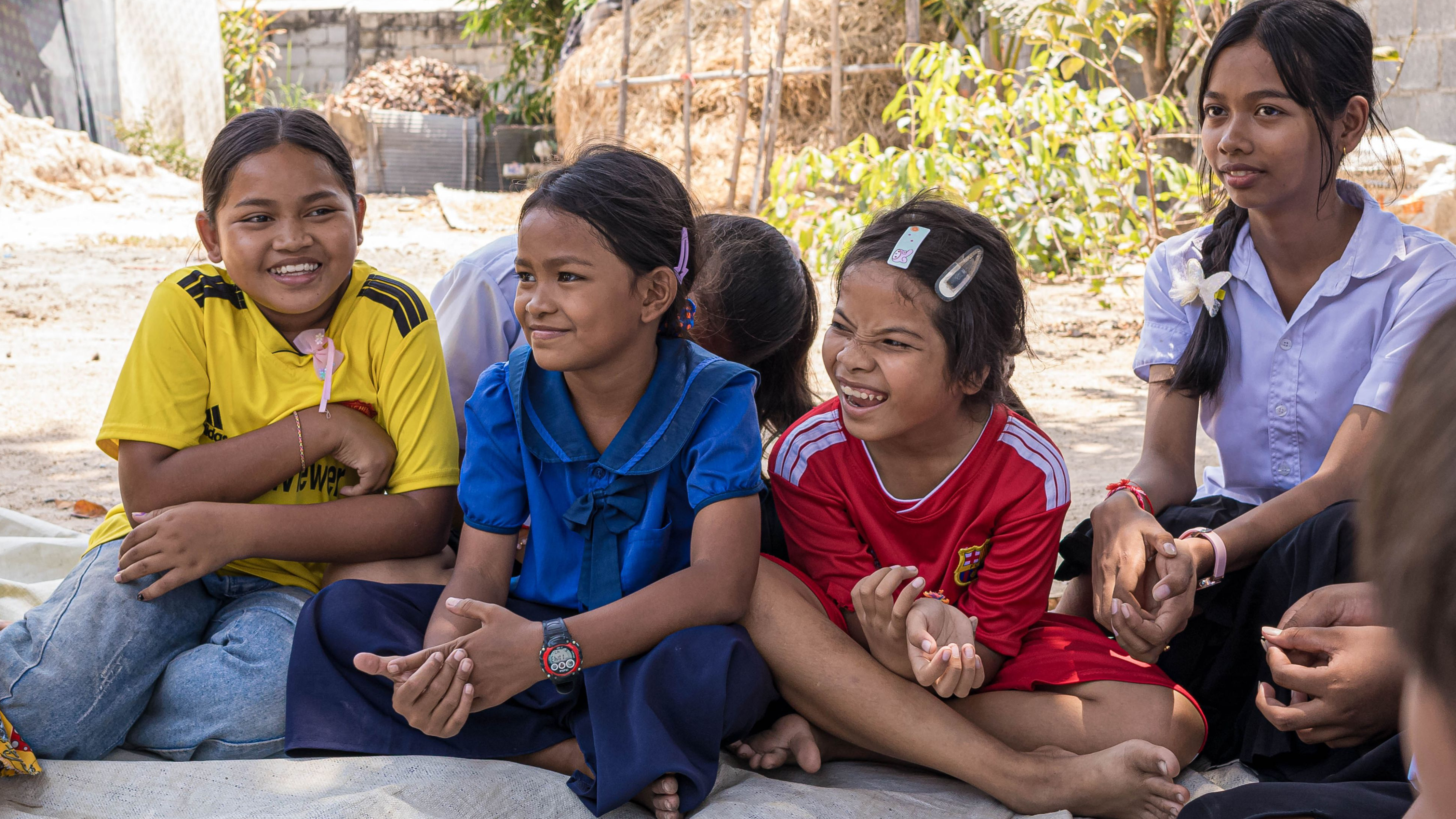 photo of 5 young girls laughing together sitting down on street