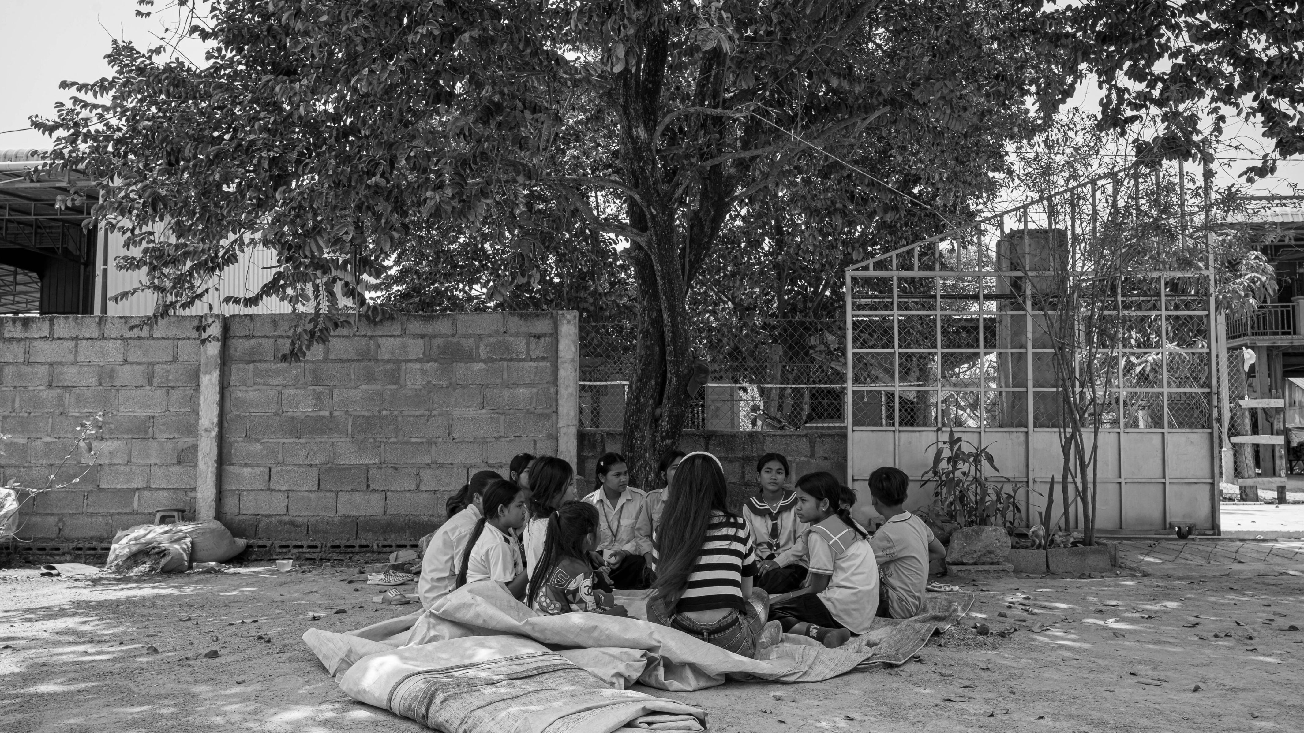 black and white photo of young girls and boys sitting in a circle behind trees